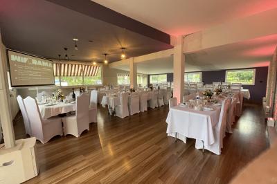 Salle de réception décorée pour un événement, avec tables rondes dressées et un écran de projection allumé.