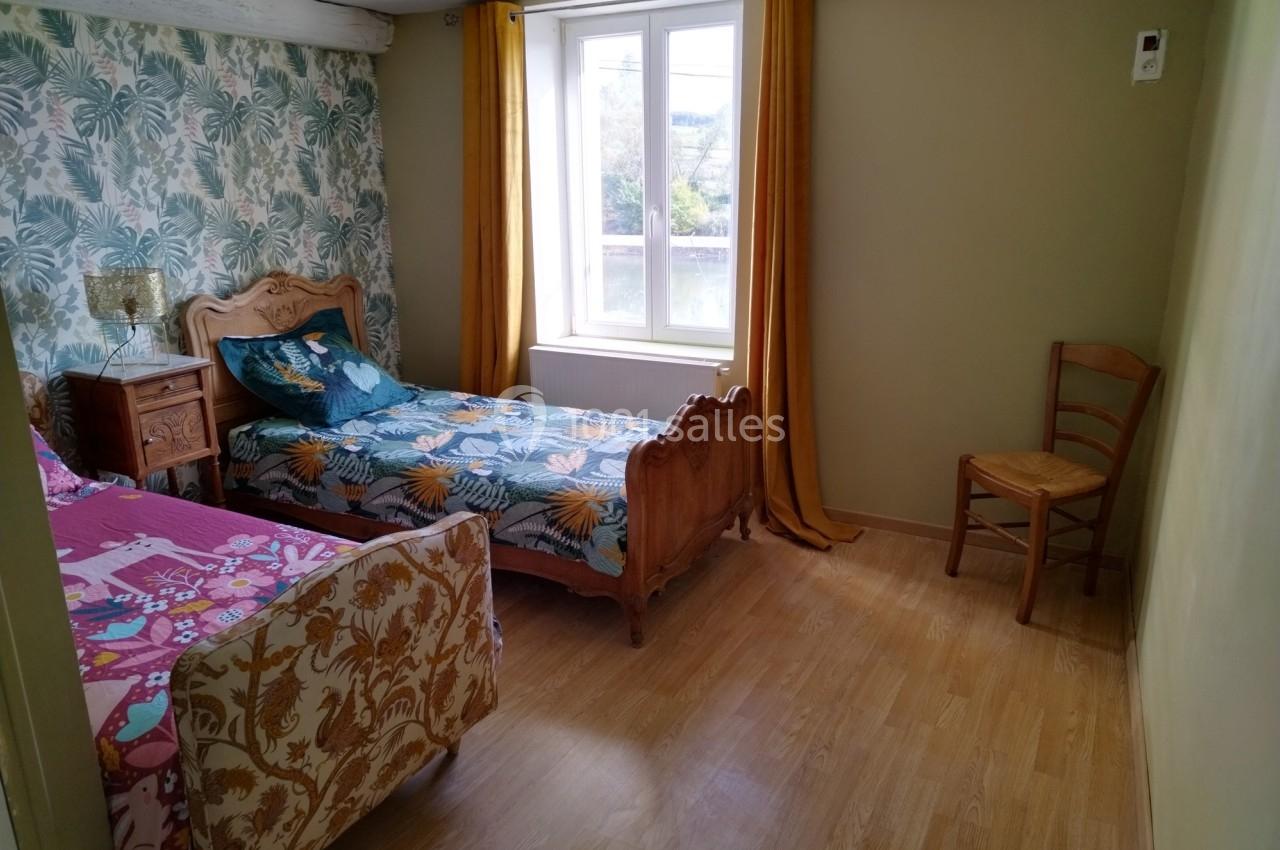 Chambre avec deux lits simples, parquet, murs clairs, papier peint à motifs, fenêtre avec rideaux jaunes.