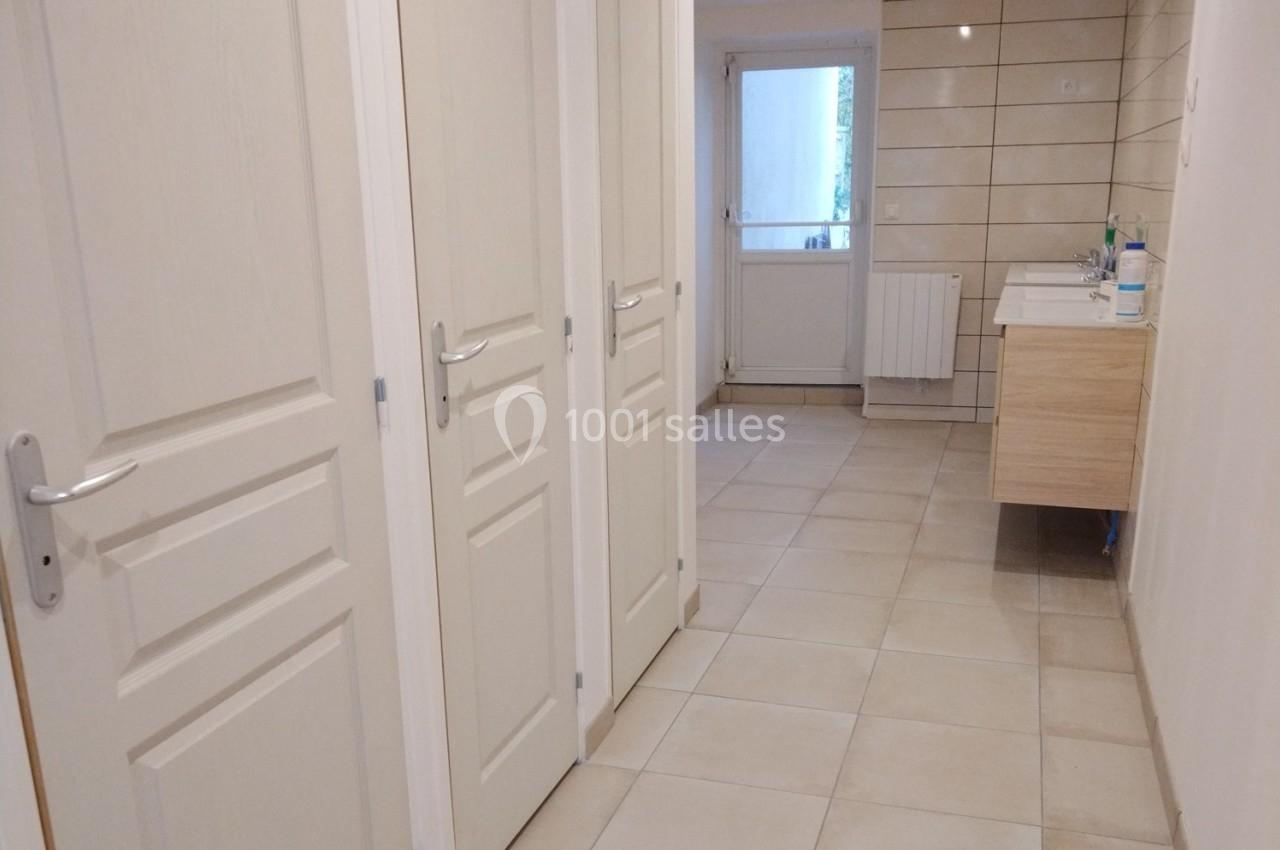 Couloir avec portes blanches menant à une salle d'eau équipée d'un lavabo et de carrelage beige au mur et au sol.