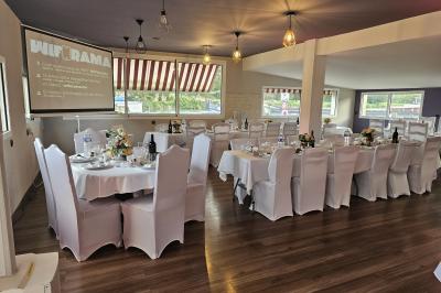 Salle de réception décorée pour un événement, avec tables rondes dressées et un écran de projection allumé.