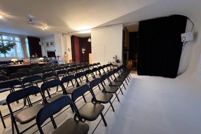 Salle avec des tables et chaises noires disposées en U, projection d’un paon coloré sur un mur blanc, rideaux noirs à droite.
