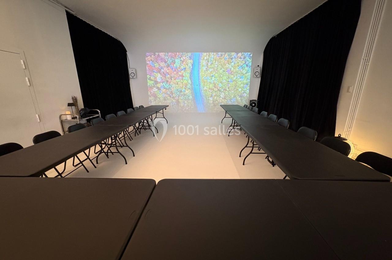 Salle de réunion avec des tables noires disposées en U, un écran projetant une image colorée en arrière-plan.