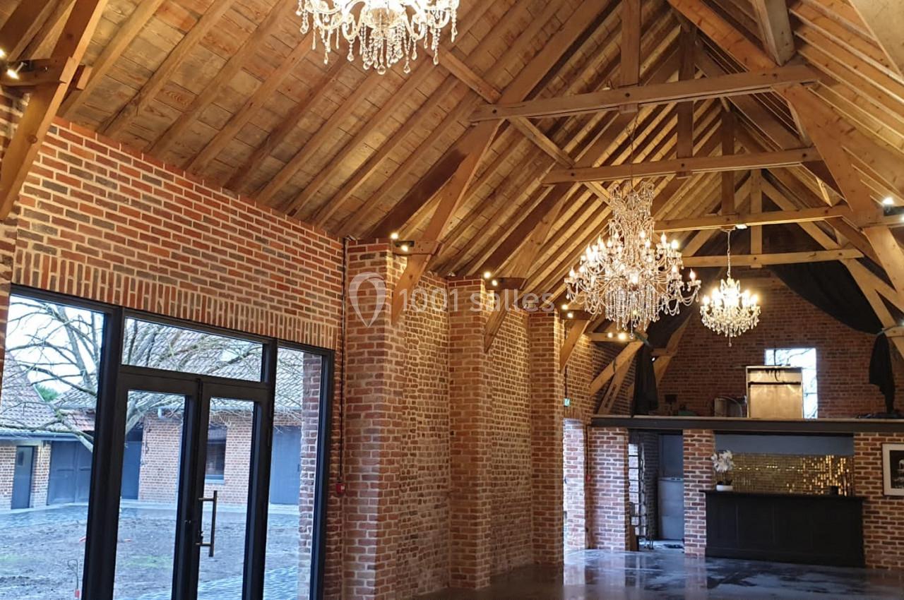 Intérieur d'une salle avec murs en briques, charpente en bois apparente et lustres suspendus.