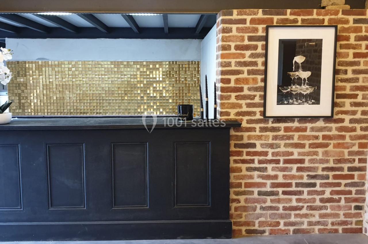 Comptoir noir devant un mur en briques, décoré d'un cadre photo, d'une orchidée blanche et d'un fond doré.