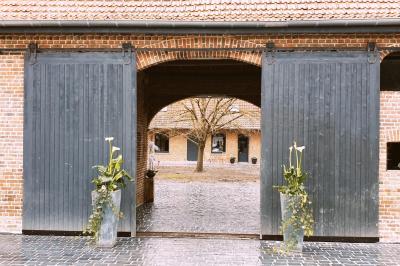 Photographie en noir et blanc d'un couple s'embrassant, la femme en robe de mariée, devant une structure en bois.