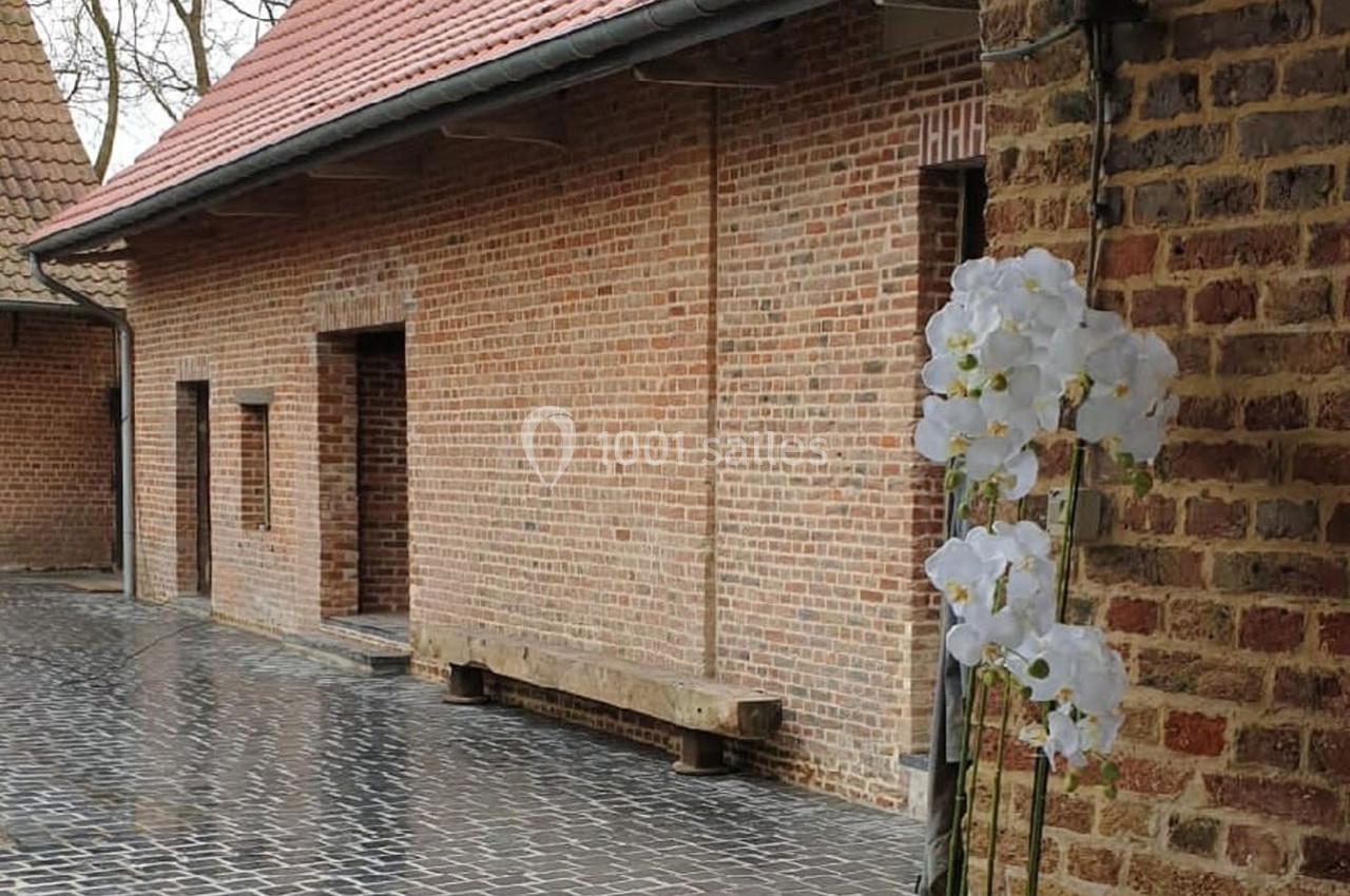 Cour pavée bordée de bâtiments en briques rouges, avec une orchidée blanche en premier plan.