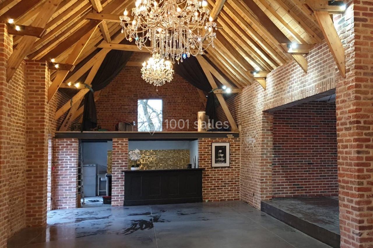 Intérieur d'une salle avec murs en briques, plafond en bois, lustres suspendus et une mezzanine au fond.