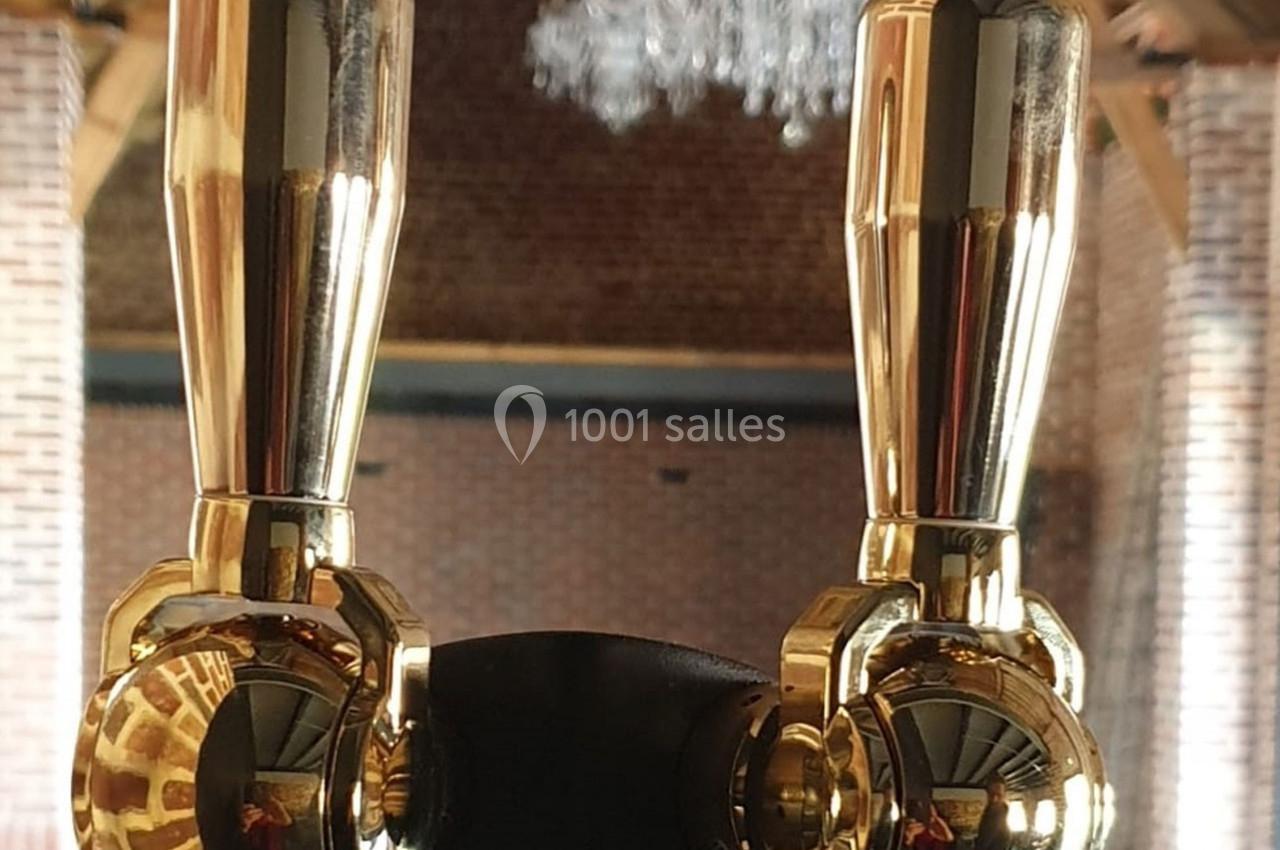 Deux robinets dorés brillants sur une tireuse à bière, avec un arrière-plan en briques et un lustre suspendu.