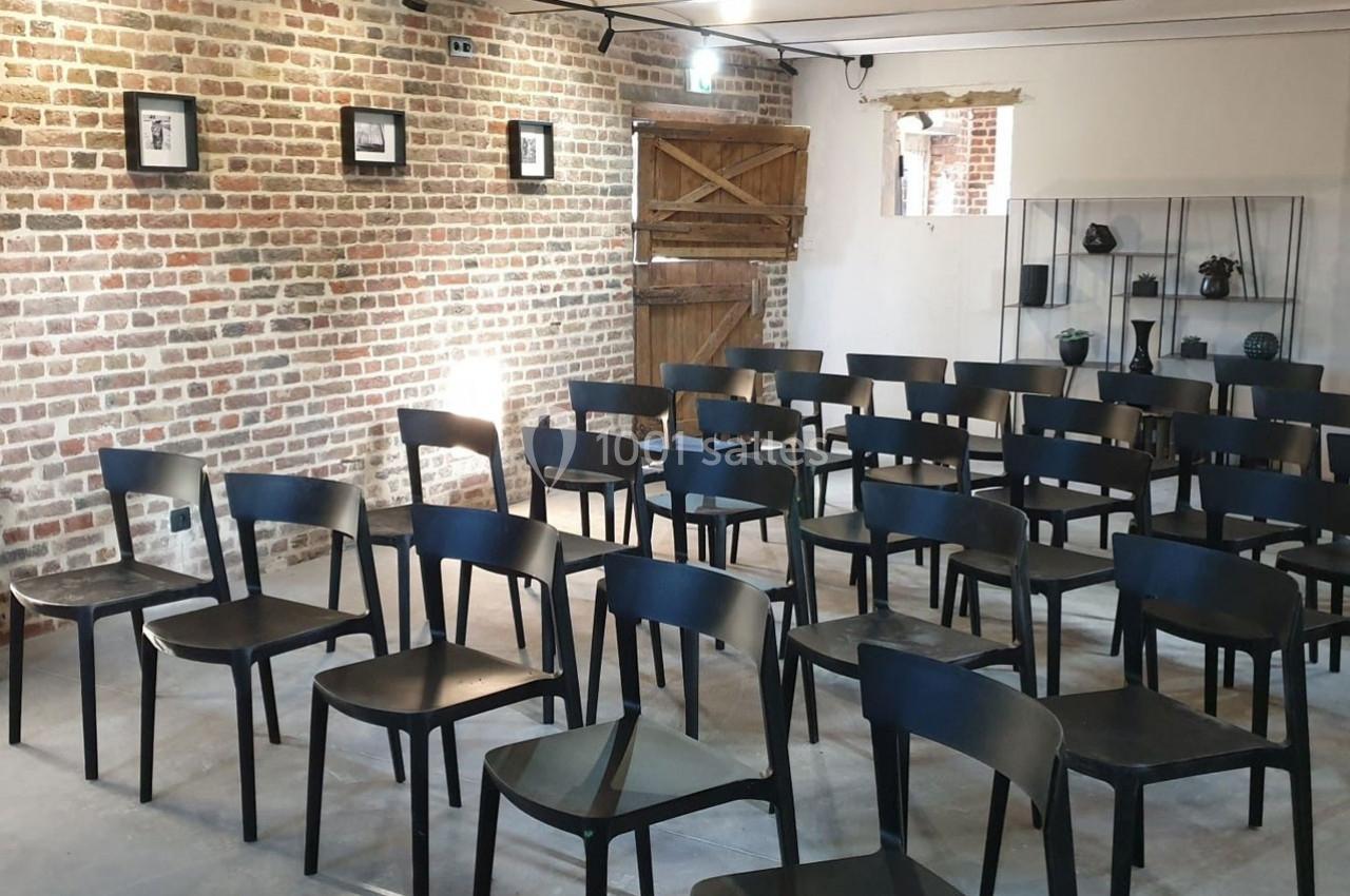 Salle avec des chaises noires alignées, murs en briques, porte en bois et étagères décoratives en arrière-plan.