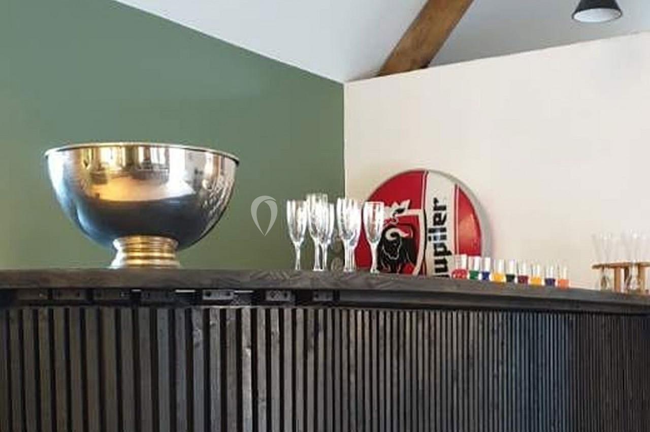 Un comptoir en bois sombre avec une grande coupe argentée, des verres et un panneau décoratif en arrière-plan.