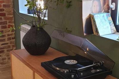 Photographie en noir et blanc d'un couple s'embrassant, la femme en robe de mariée, devant une structure en bois.