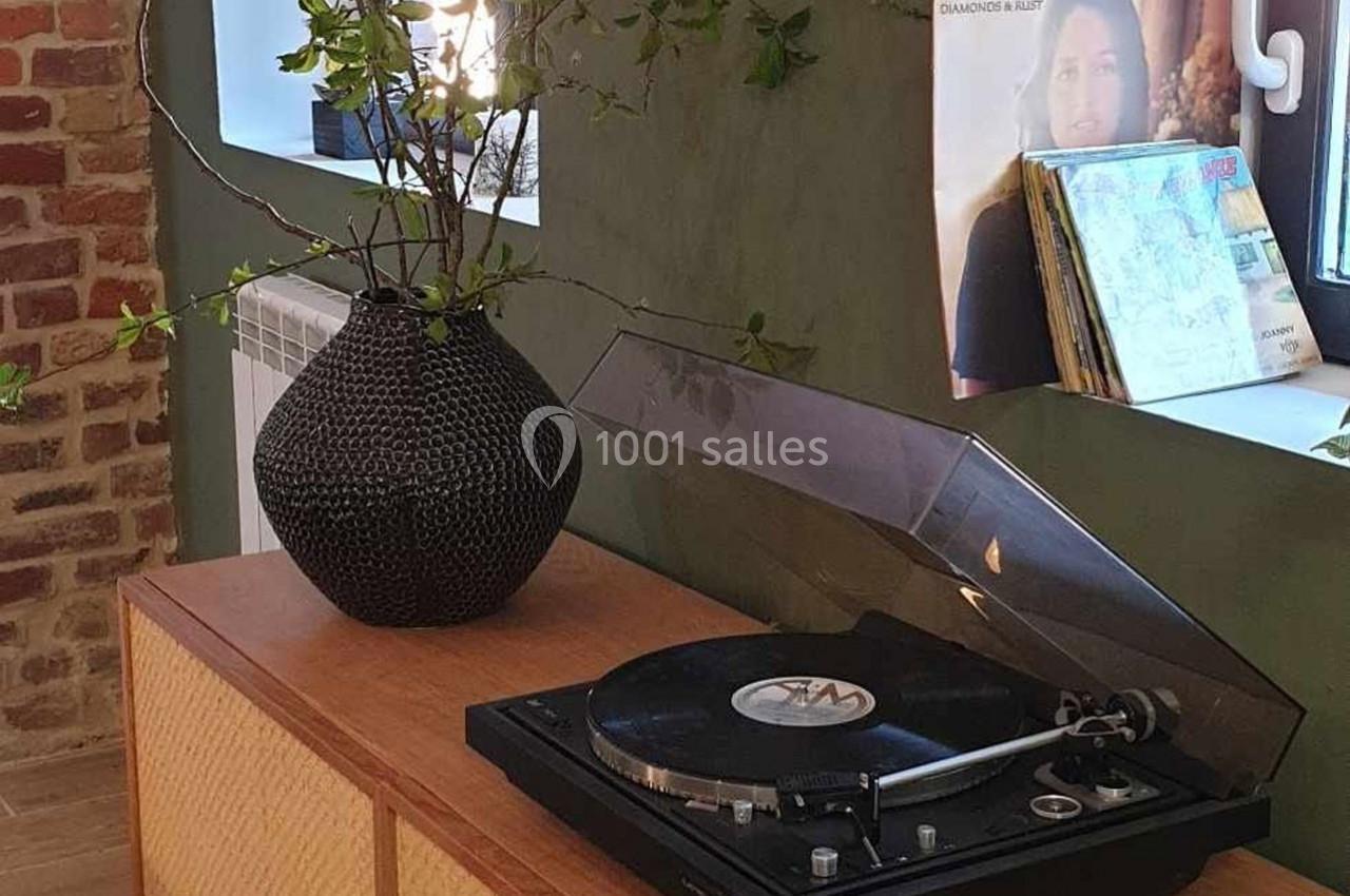 Platine vinyle sur un meuble en bois, avec un vase noir et des branches, près d'une fenêtre et d'une affiche.