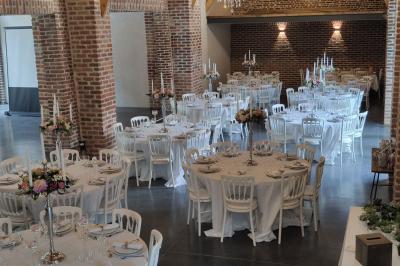 Photographie en noir et blanc d'un couple s'embrassant, la femme en robe de mariée, devant une structure en bois.