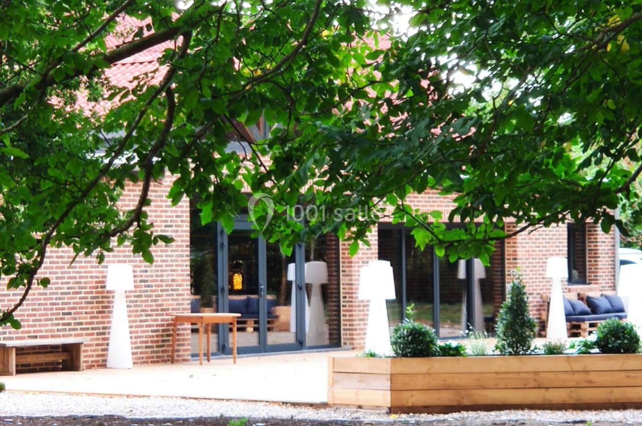 Façade en briques d'une maison avec terrasse aménagée, entourée de verdure et de jardinières en bois.