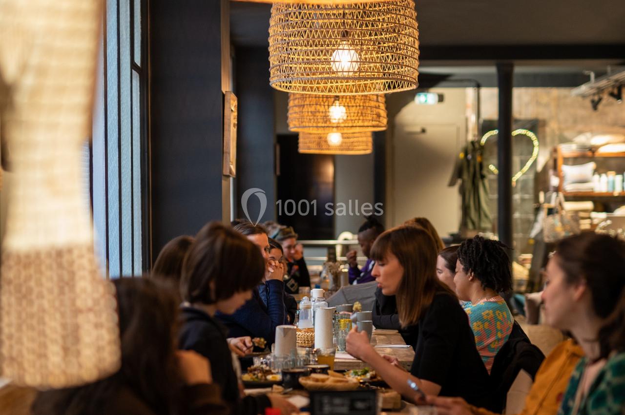 Des personnes dînent dans un restaurant à l'ambiance chaleureuse, éclairé par des suspensions en osier.