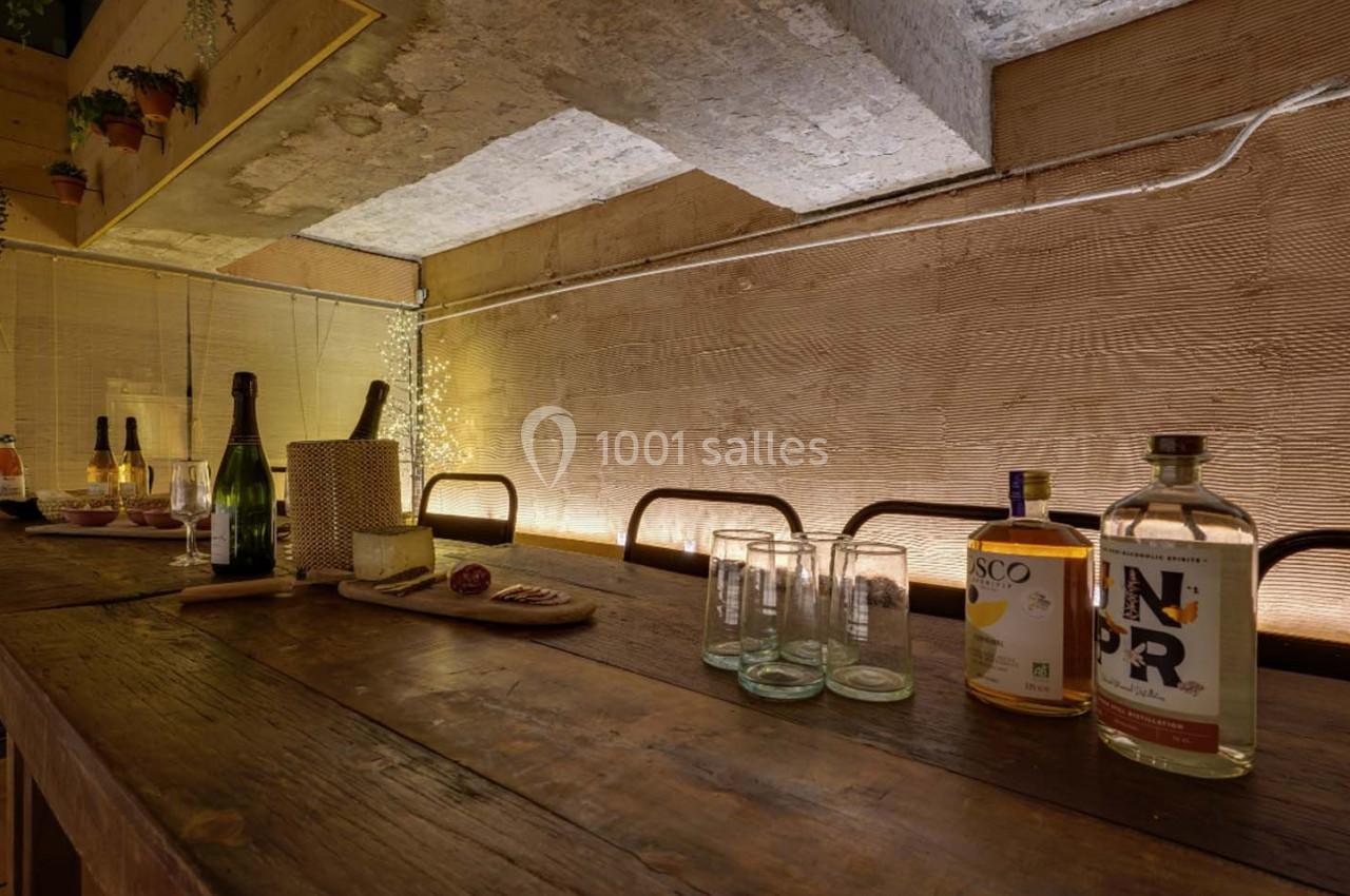 Table en bois avec bouteilles, verres et planche apéritive, dans un espace intérieur à l'éclairage tamisé.