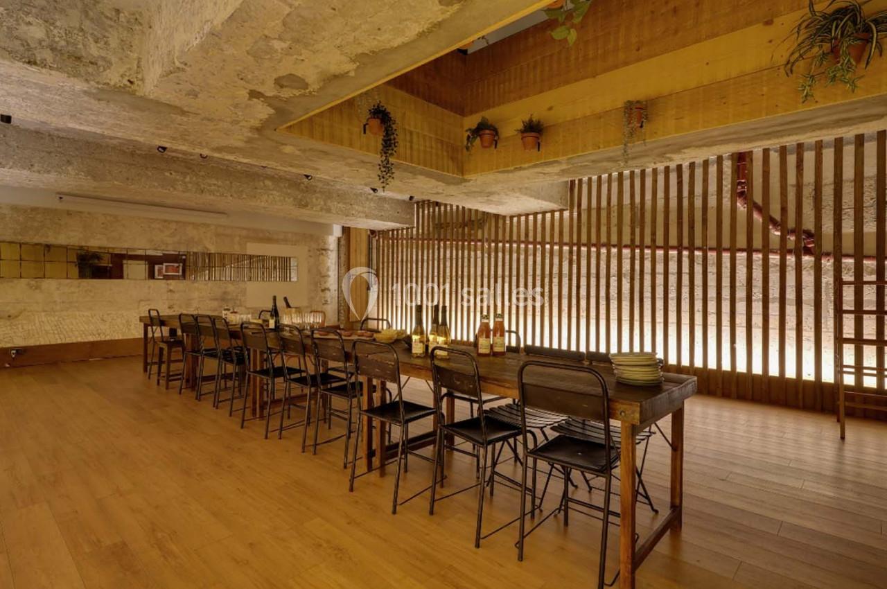Salle à manger avec une grande table en bois, des chaises métalliques, un éclairage chaleureux et des plantes suspendues.