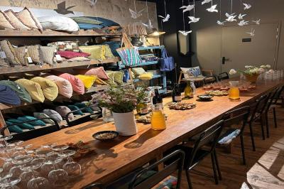 Table en bois dressée avec boissons, fleurs et collations, entourée d'étagères garnies de coussins colorés et décorations.