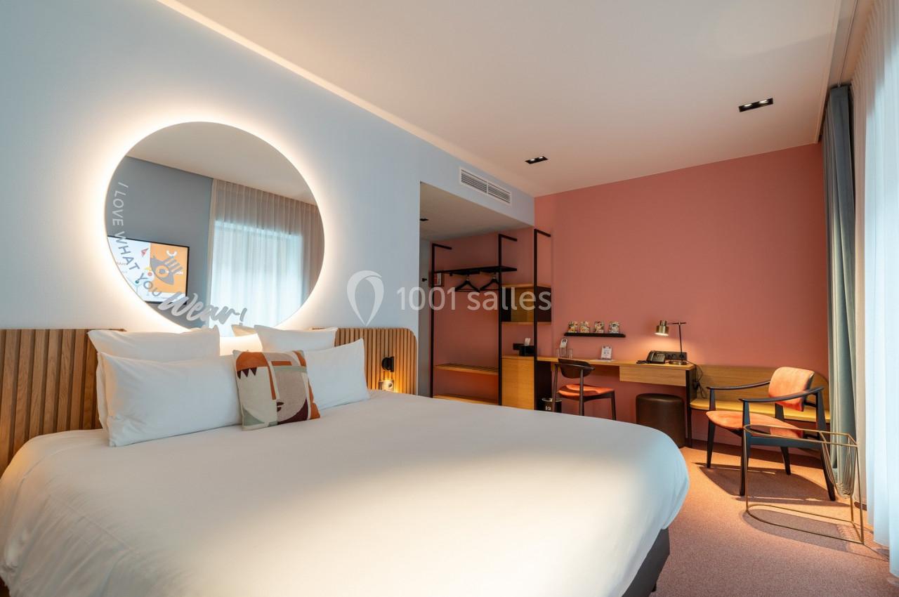 Chambre d'hôtel moderne avec lit double, bureau, chaise et éclairage doux, décorée dans des tons clairs et chaleureux.