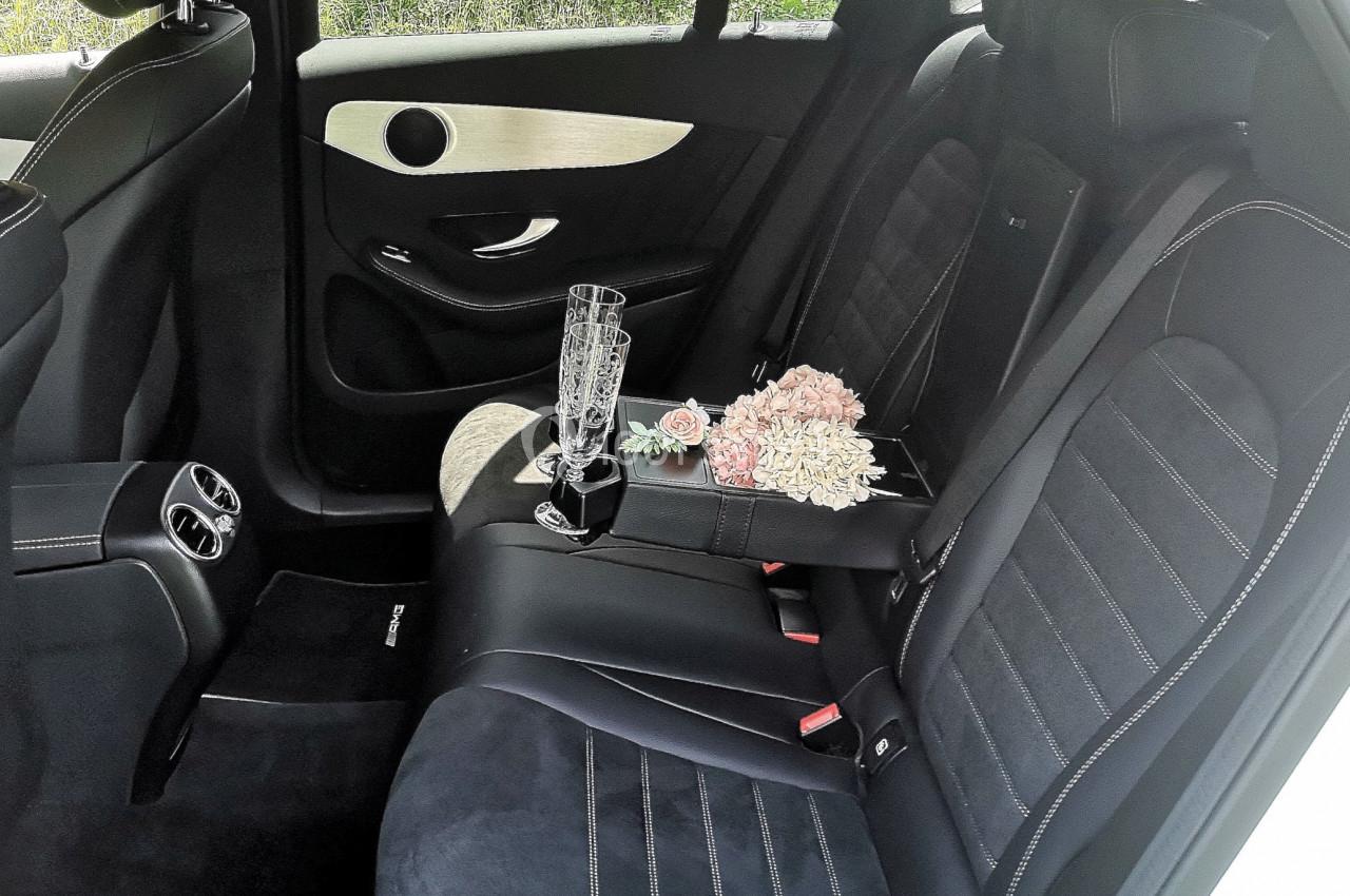 Intérieur d'une voiture avec sièges en cuir noir, un bouquet de fleurs et deux flûtes à champagne sur l'accoudoir.