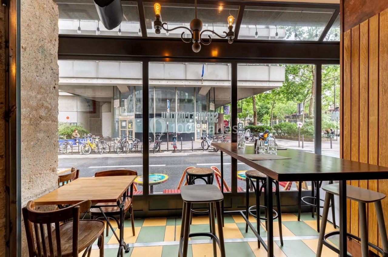 Intérieur d'un café avec des tables en bois, vue sur une rue avec des vélos et un bâtiment moderne à travers une baie vitrée.