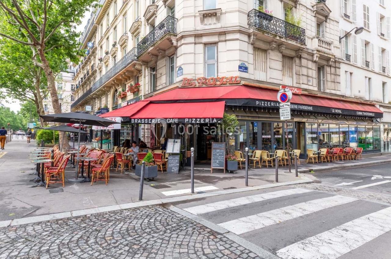 Terrasse d'une brasserie parisienne avec des tables et chaises colorées, située à l'angle d'une rue calme.