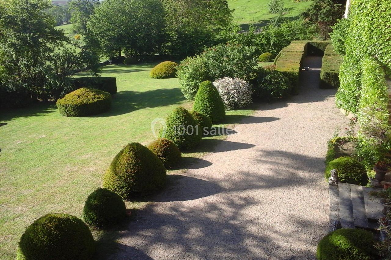Allée bordée de buissons taillés et pelouse verdoyante dans un jardin paysager ensoleillé.