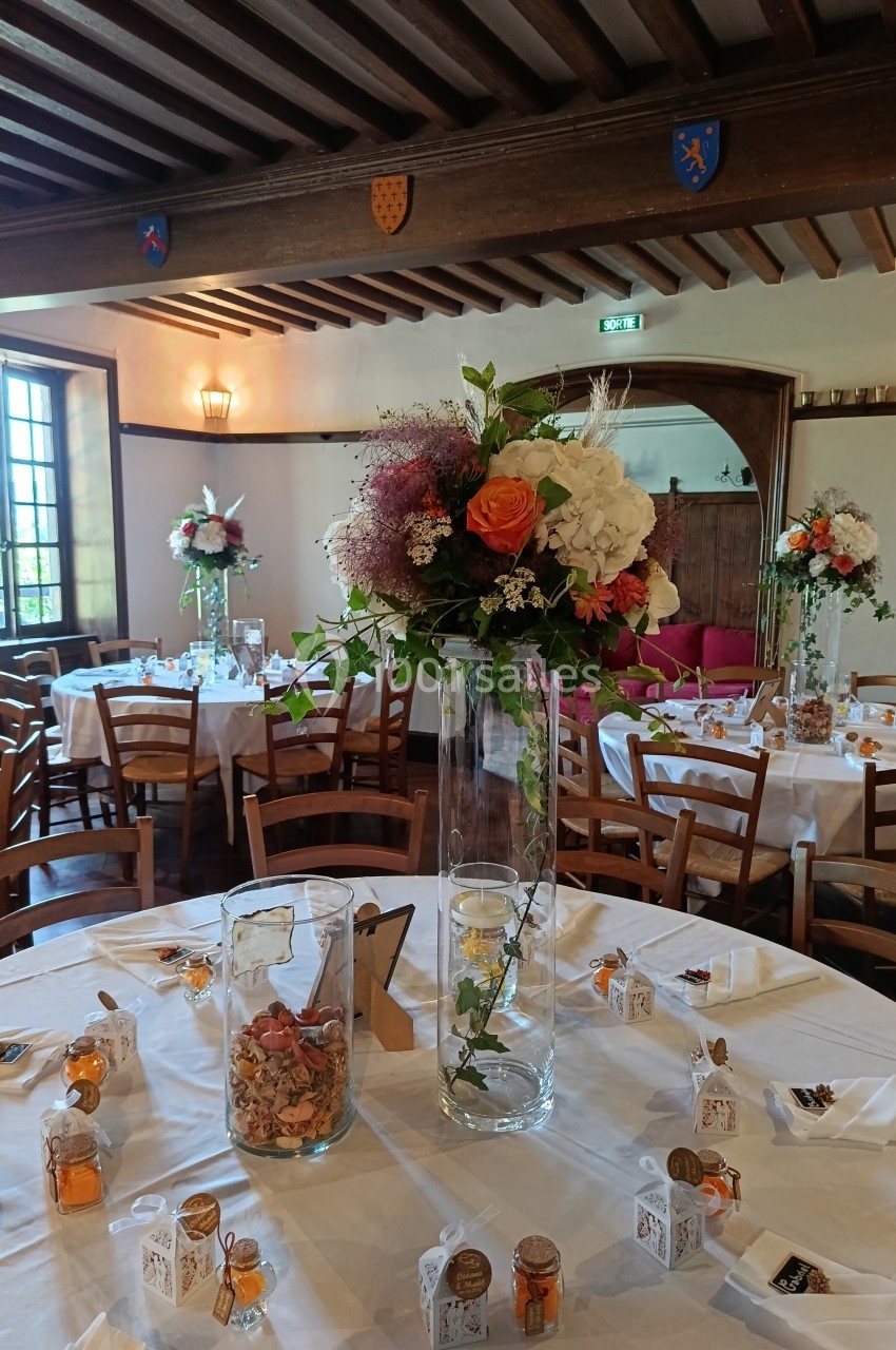 Salle de réception décorée avec des tables dressées, ornées de bouquets de fleurs et de petits cadeaux.
