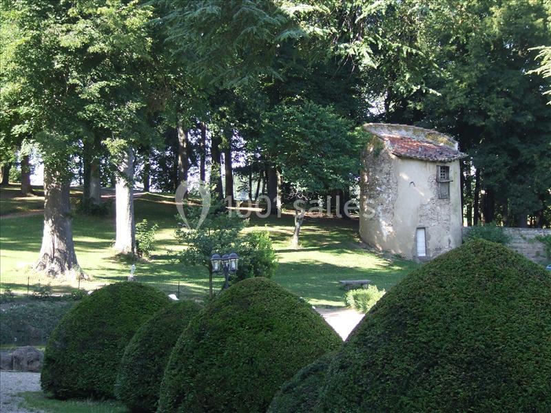 Petite maison en pierre entourée d'arbres dans un parc avec des buissons taillés au premier plan.
