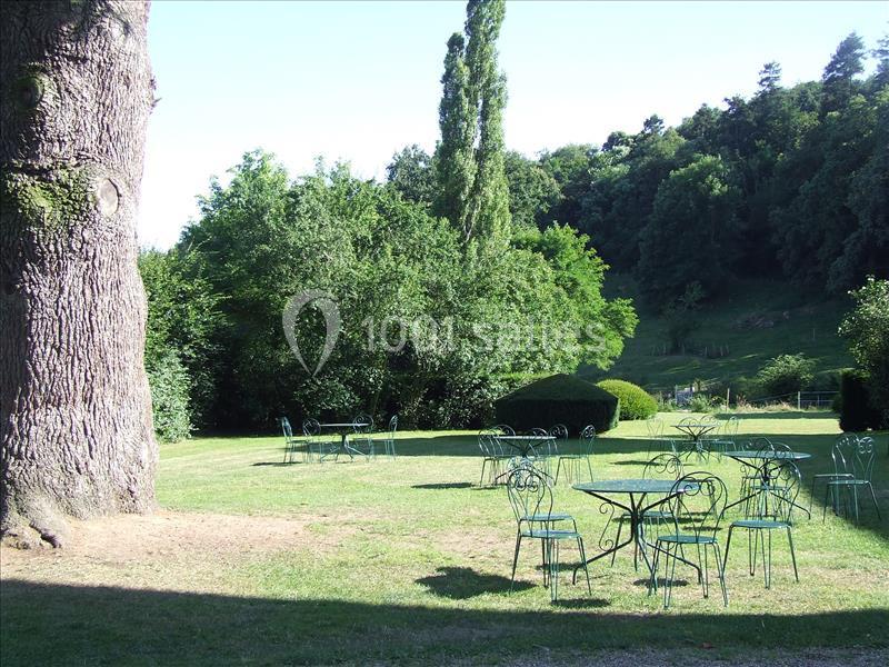 Chaises et tables en métal vert disposées sur une pelouse, entourées d'arbres et de végétation dense.
