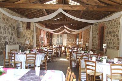 Salle de restaurant avec tables rondes dressées, nappes blanches, chaises en bois et éclairage tamisé.