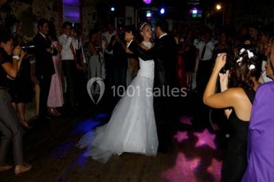 Salle de restaurant avec tables rondes dressées, nappes blanches, chaises en bois et éclairage tamisé.