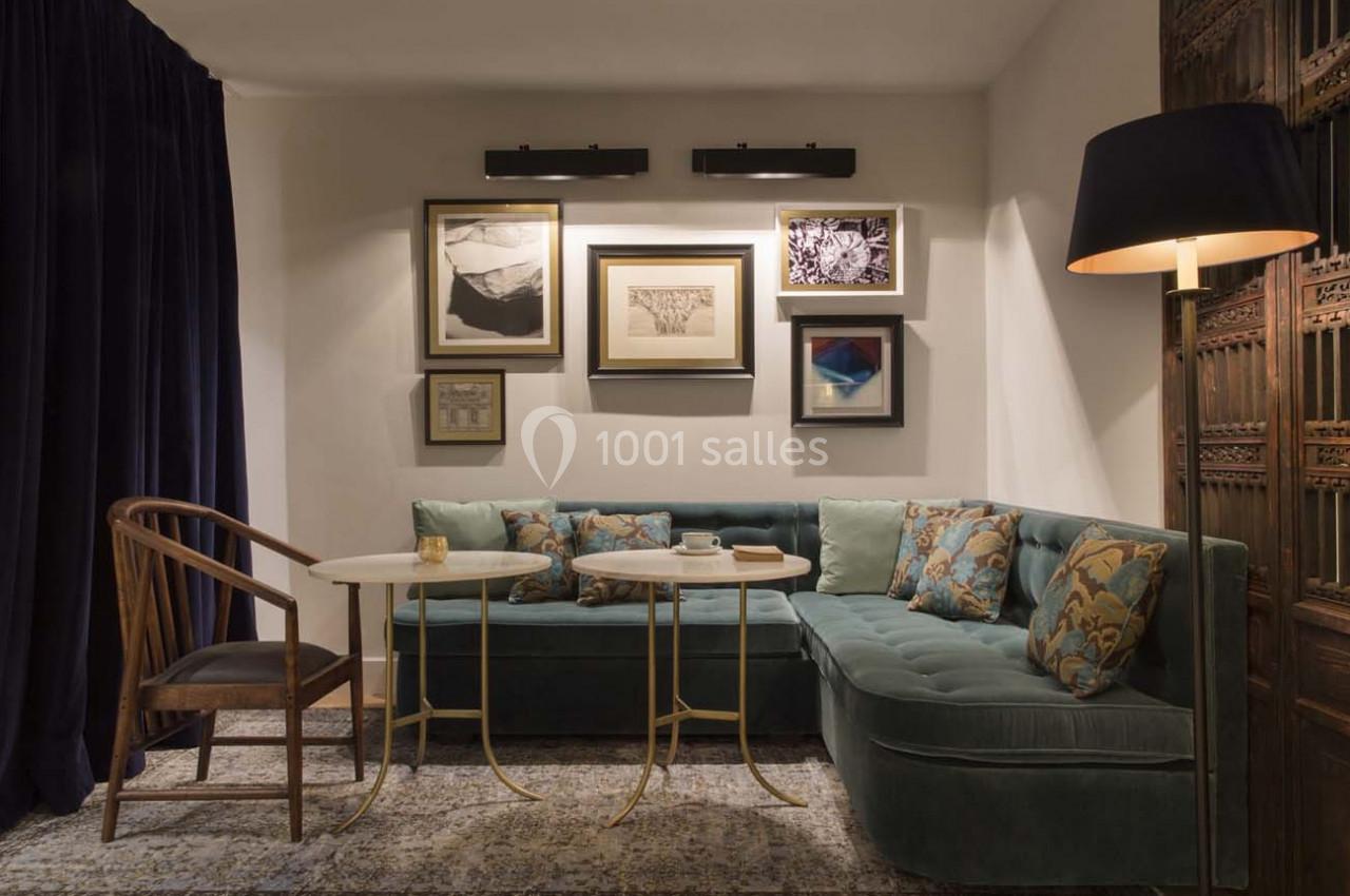 Coin salon avec canapé d'angle vert, tables basses, chaise en bois, lampadaire et mur décoré de cadres.