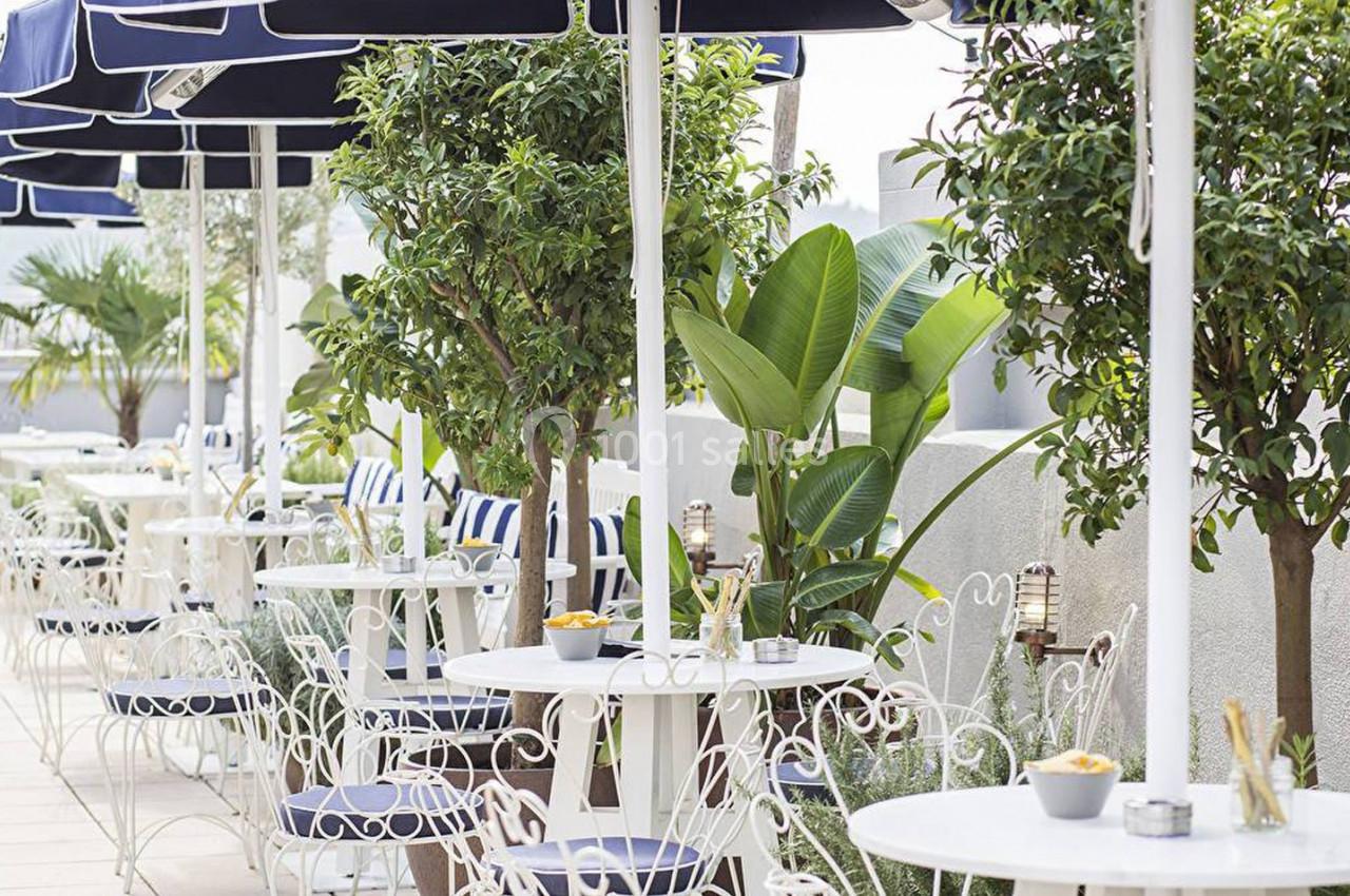 Terrasse extérieure avec tables et chaises blanches, parasols noirs et végétation luxuriante.