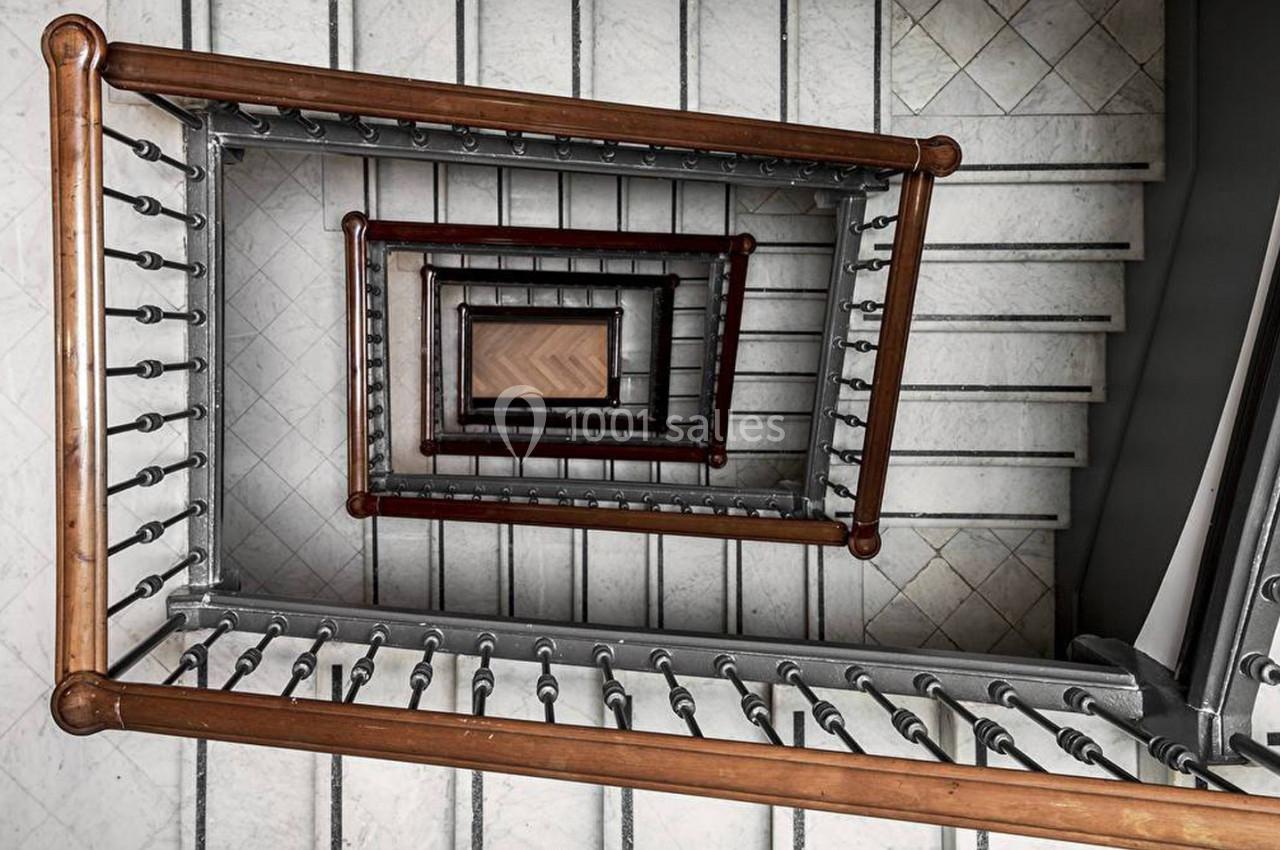 Vue plongeante d'une cage d'escalier en colimaçon avec rambardes en métal et marches en bois.