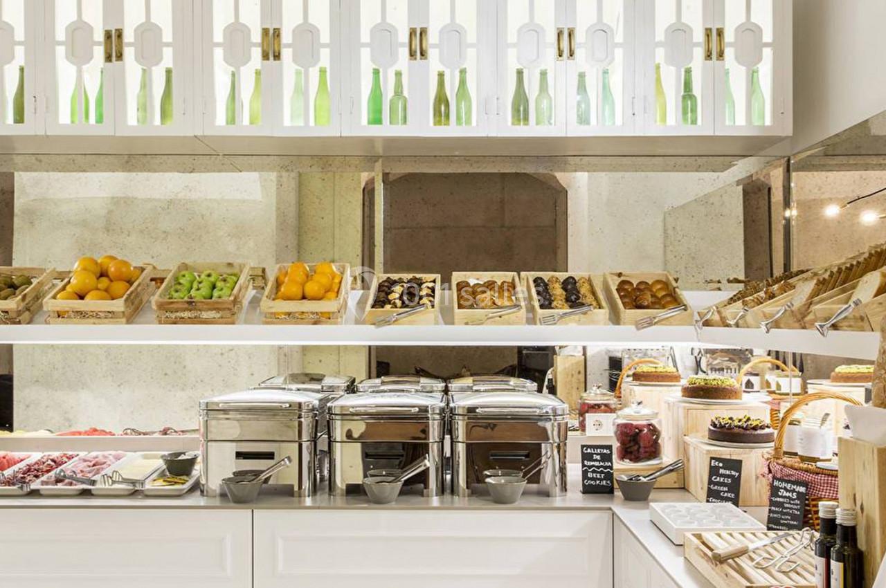 Buffet de petit-déjeuner avec fruits, viennoiseries, pains, plats chauds et boissons disposés sur un comptoir lumineux.