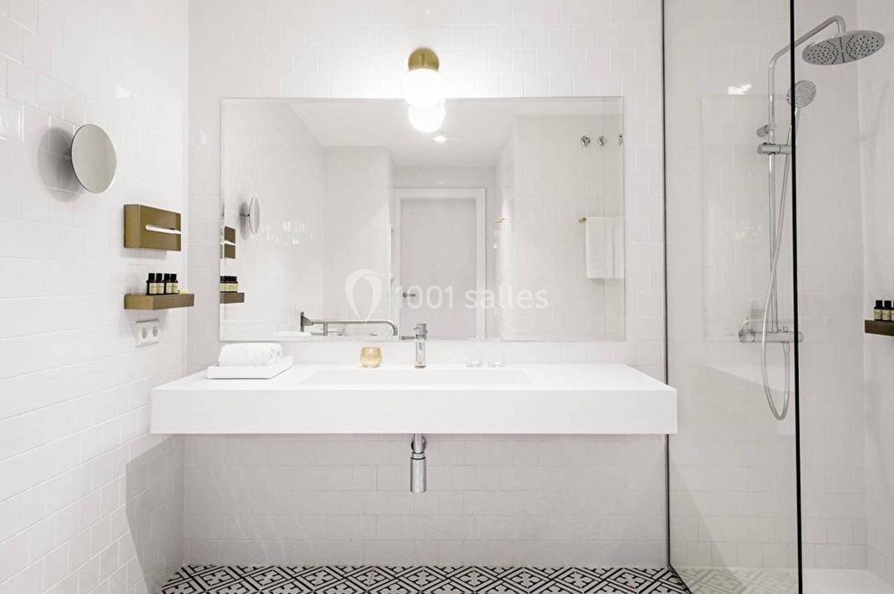Salle de bain moderne avec lavabo blanc, miroir mural, douche vitrée et carrelage au sol à motifs géométriques.