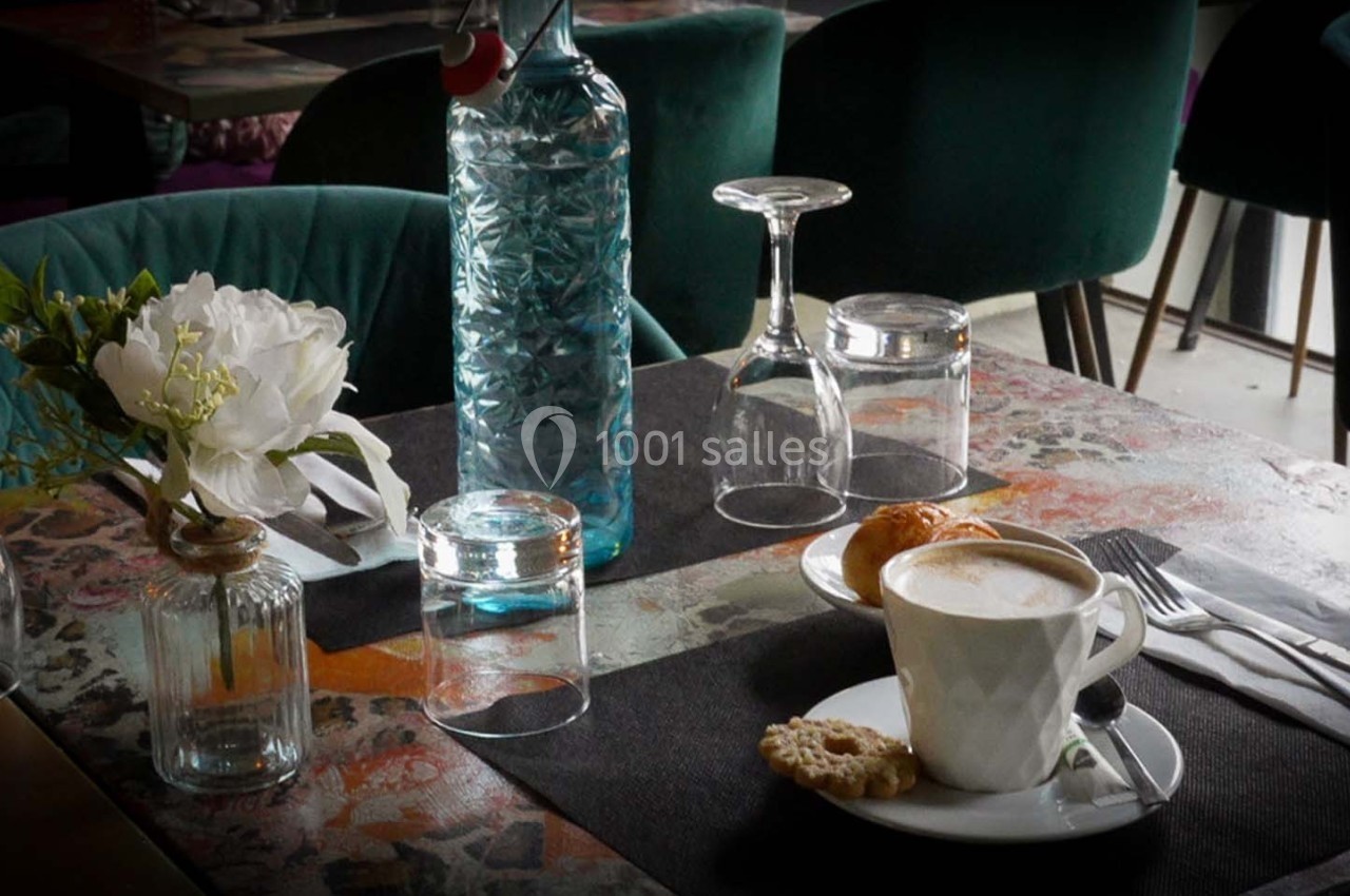 Table de café avec une tasse de cappuccino, un biscuit, une bouteille d'eau, des verres et une fleur en vase.