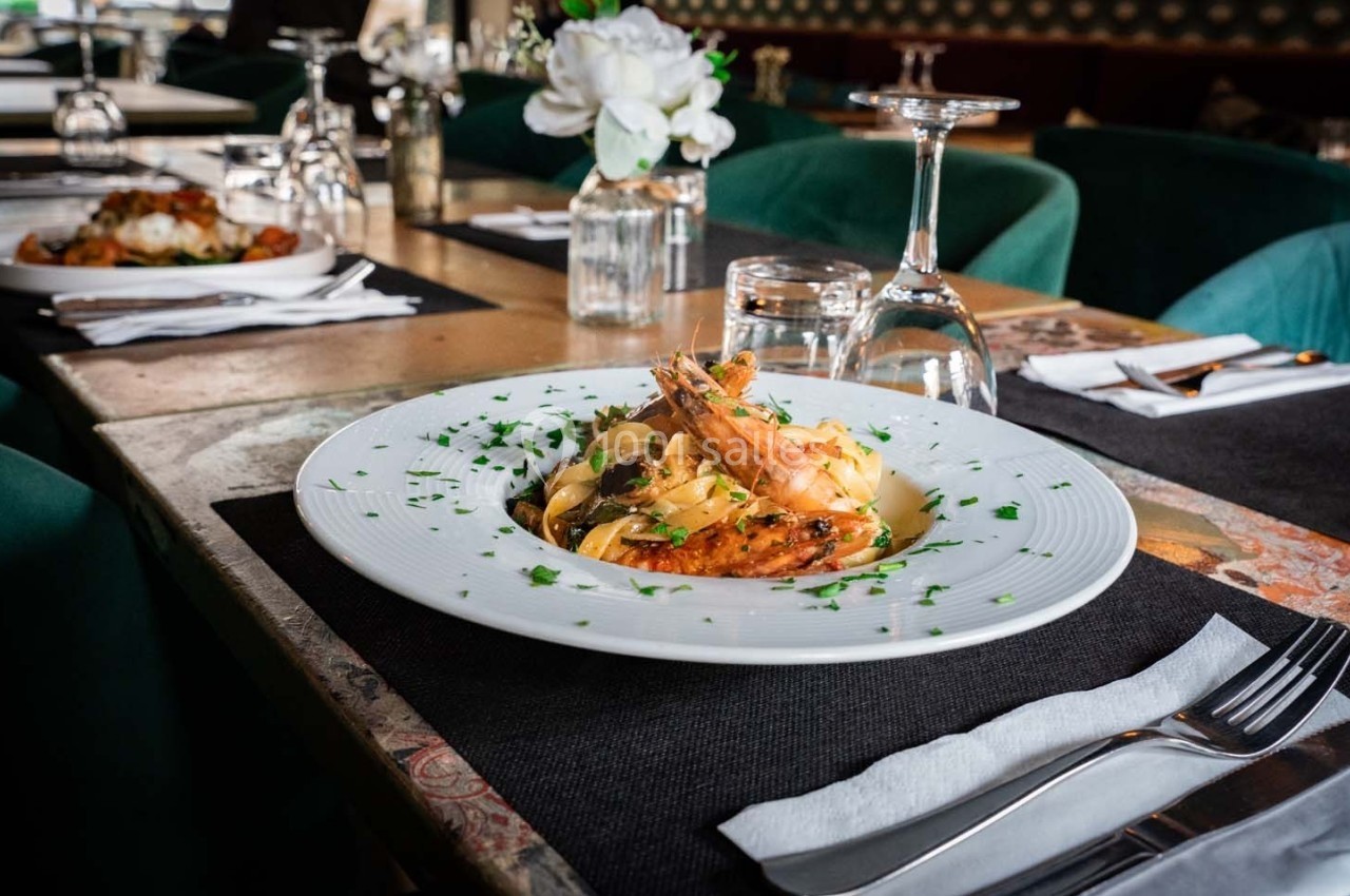 Assiette de pâtes garnie de crevettes et herbes fraîches, servie sur une table dressée dans un restaurant élégant.