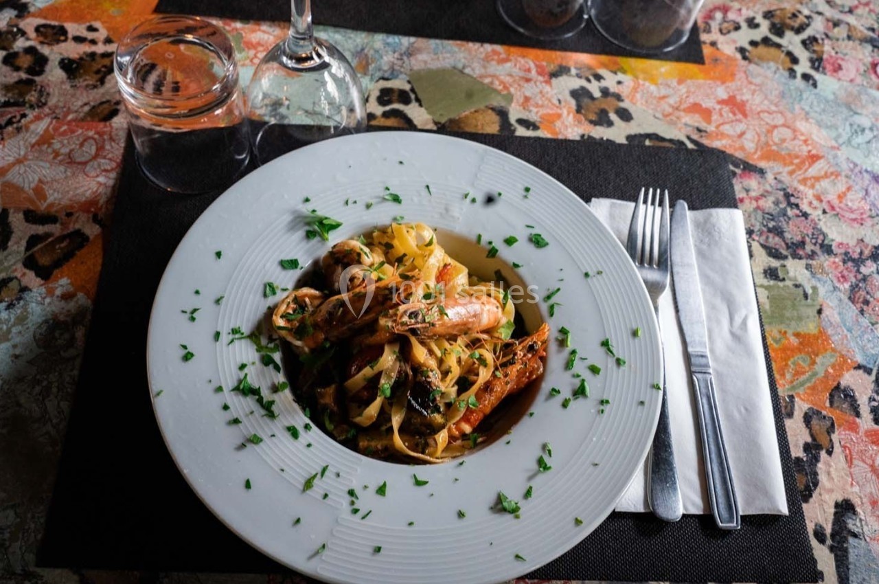 Assiette de tagliatelles aux fruits de mer, garnie de crevettes et persil, servie sur une table colorée.
