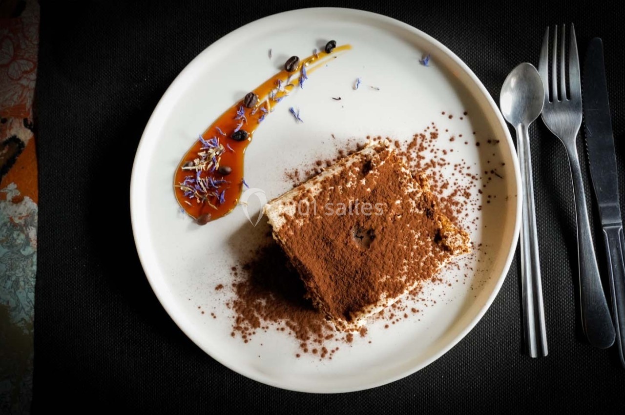 Dessert au cacao saupoudré, accompagné d'une sauce caramel décorée de fleurs et servi sur une assiette blanche.
