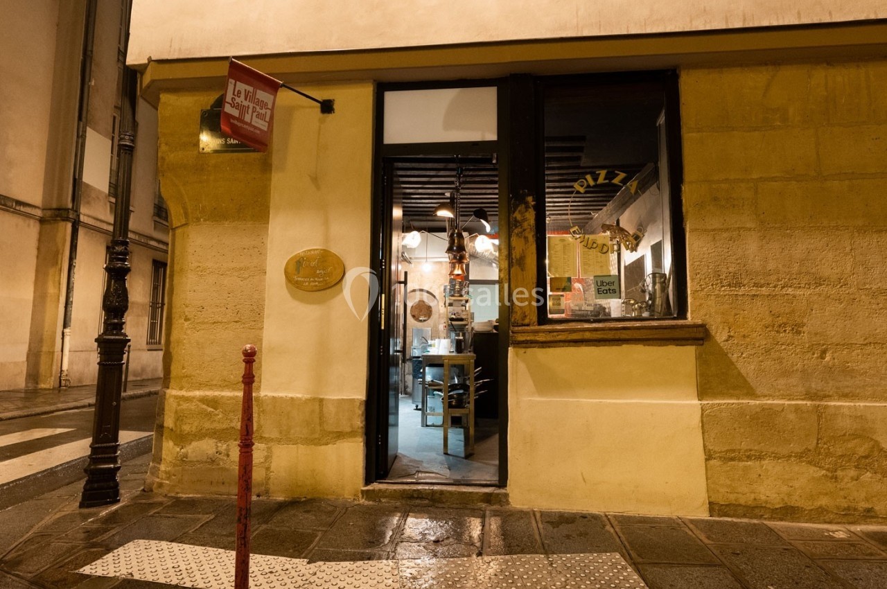 Façade d'un petit restaurant éclairé la nuit, avec une porte vitrée et un trottoir humide devant.