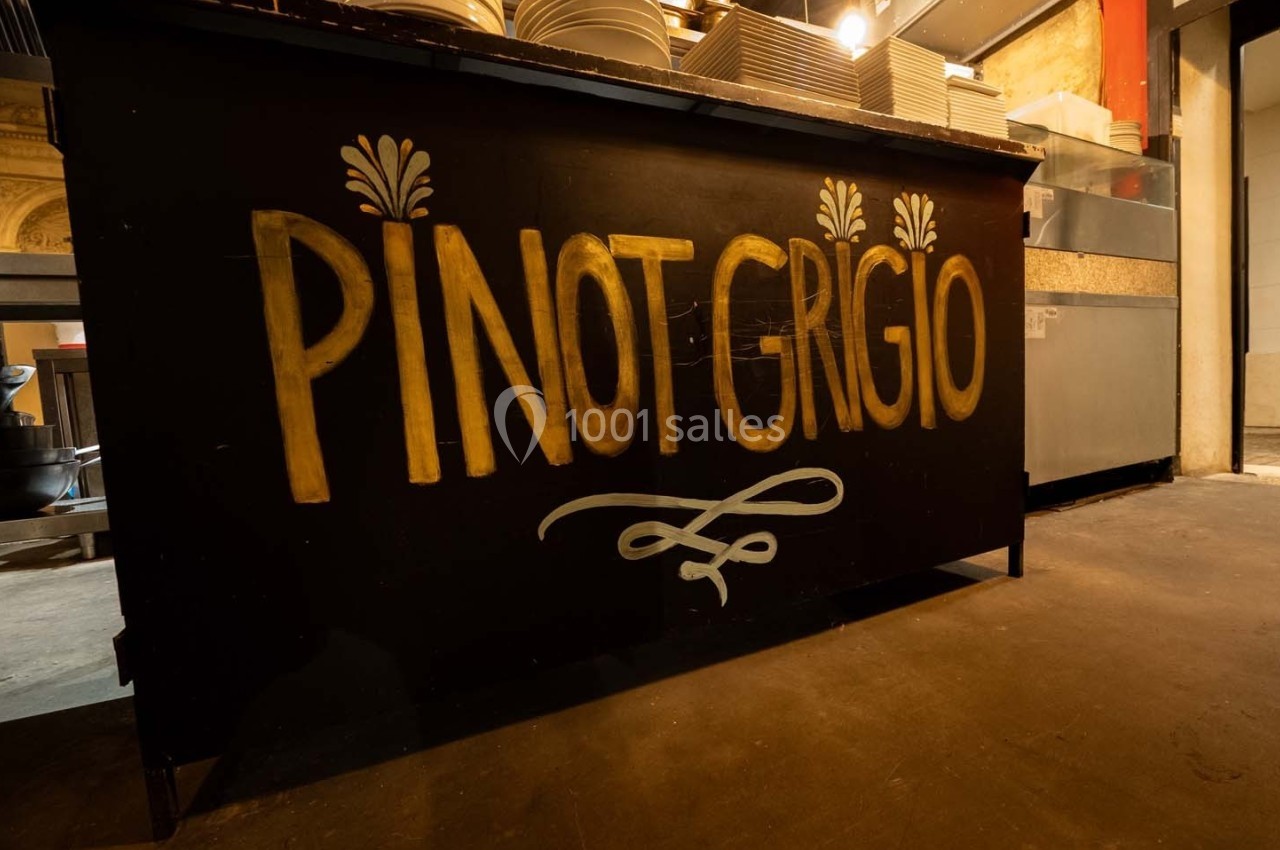 Comptoir noir avec l'inscription ’Pinot Grigio’ en lettres dorées, situé dans un espace intérieur avec vaisselle en arrière…