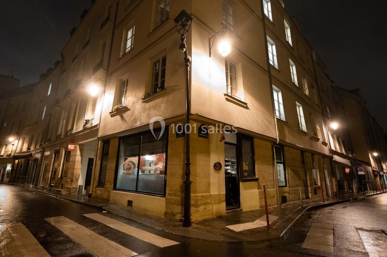 Coin de rue parisienne la nuit, éclairé par des lampadaires, avec des bâtiments anciens et des fenêtres illuminées.