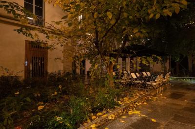 Cour intérieure éclairée de nuit, avec des chaises et tables sous un arbre aux feuilles jaunies en automne.