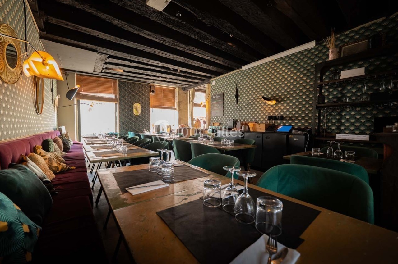 Salle de restaurant avec tables en bois, chaises vertes, banquettes violettes et décoration murale rétro.