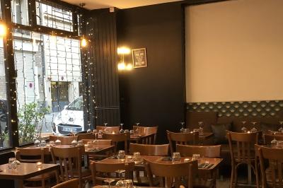 Cour intérieure éclairée de nuit, avec des chaises et tables sous un arbre aux feuilles jaunies en automne.
