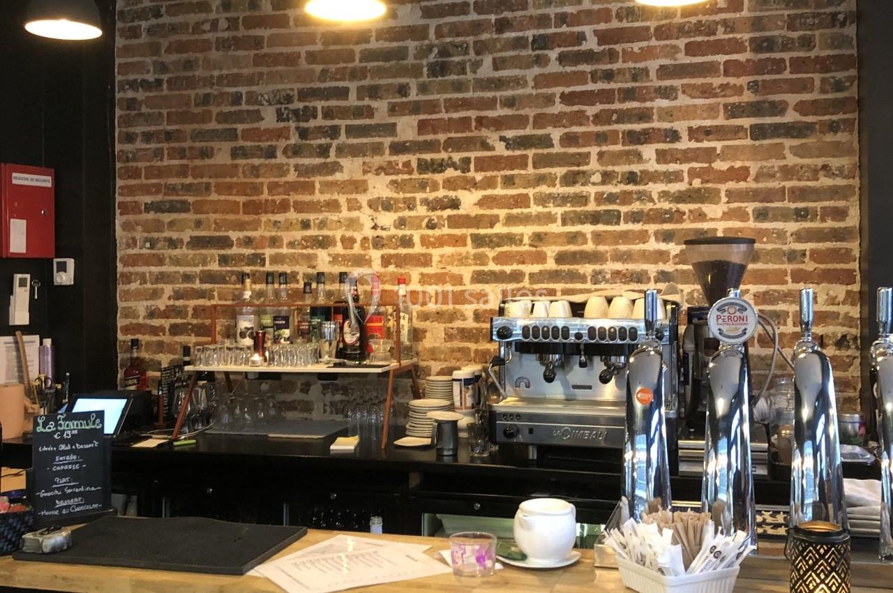 Comptoir de café avec machine à expresso, tireuses à bière, tasses et mur en briques en arrière-plan.