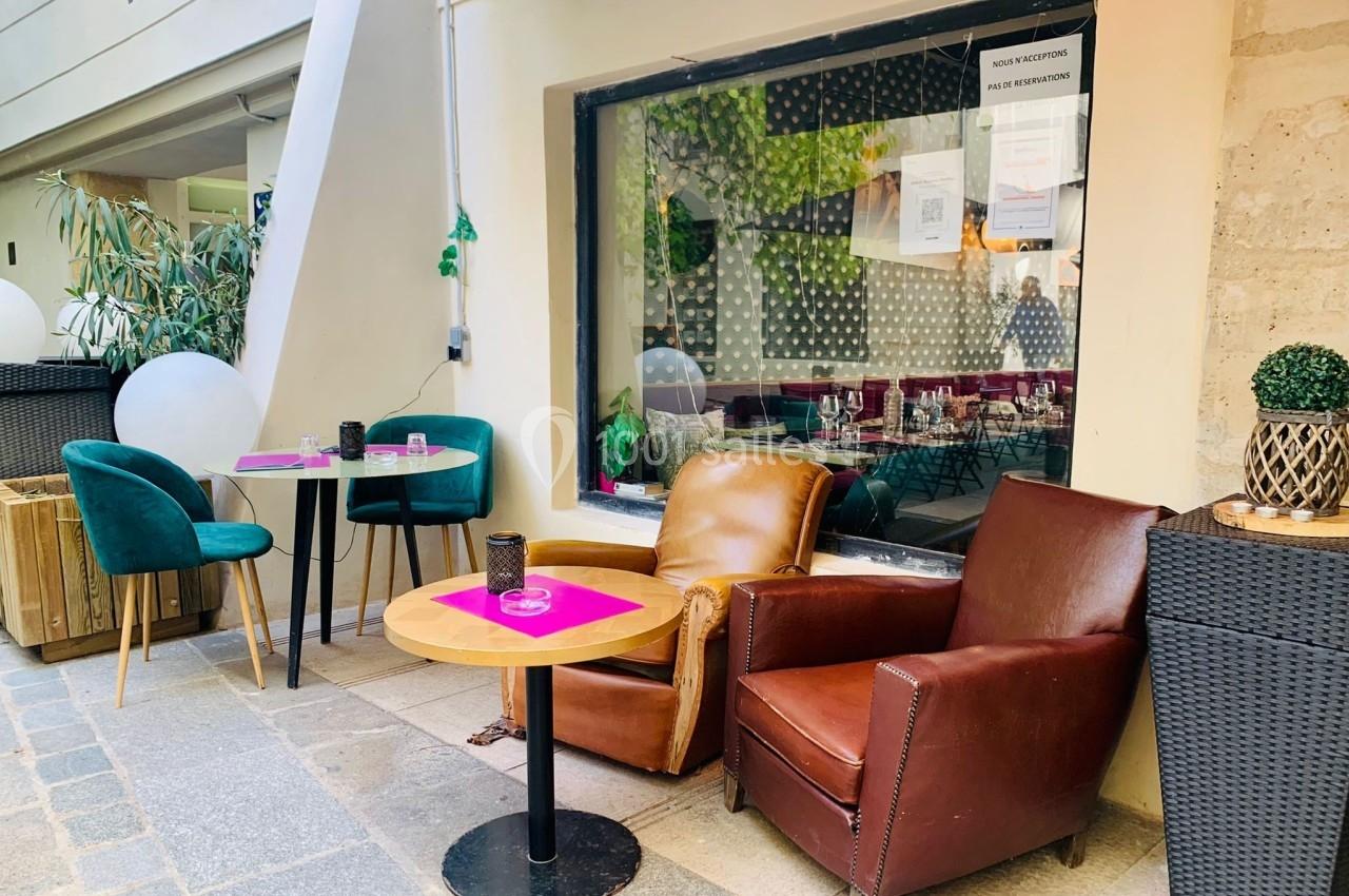 Terrasse avec fauteuils en cuir, tables basses et décor végétal, située devant une vitrine de restaurant.