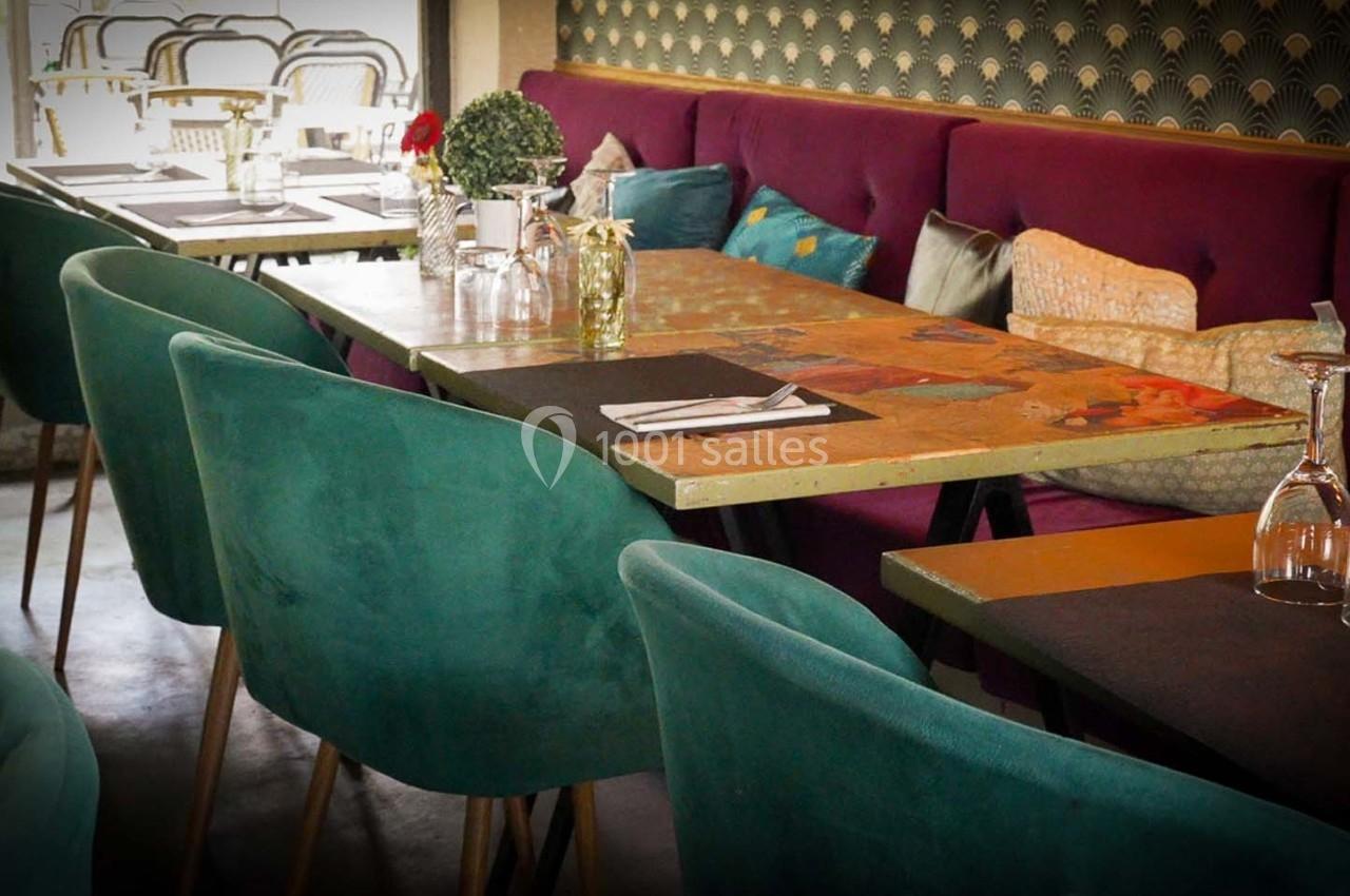 Salle de restaurant avec tables en bois, chaises vertes et banquette violette, décorée de coussins et plantes.
